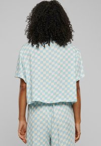 Blå og hvit rutete crop top med avslappet passform, korte ermer og rund kant, laget av glatt stoff.