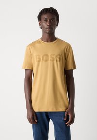 Mustard yellow cotton t-shirt with short sleeves and a crew neckline, featuring a large, tonal "BOSS" logo printed on the front.