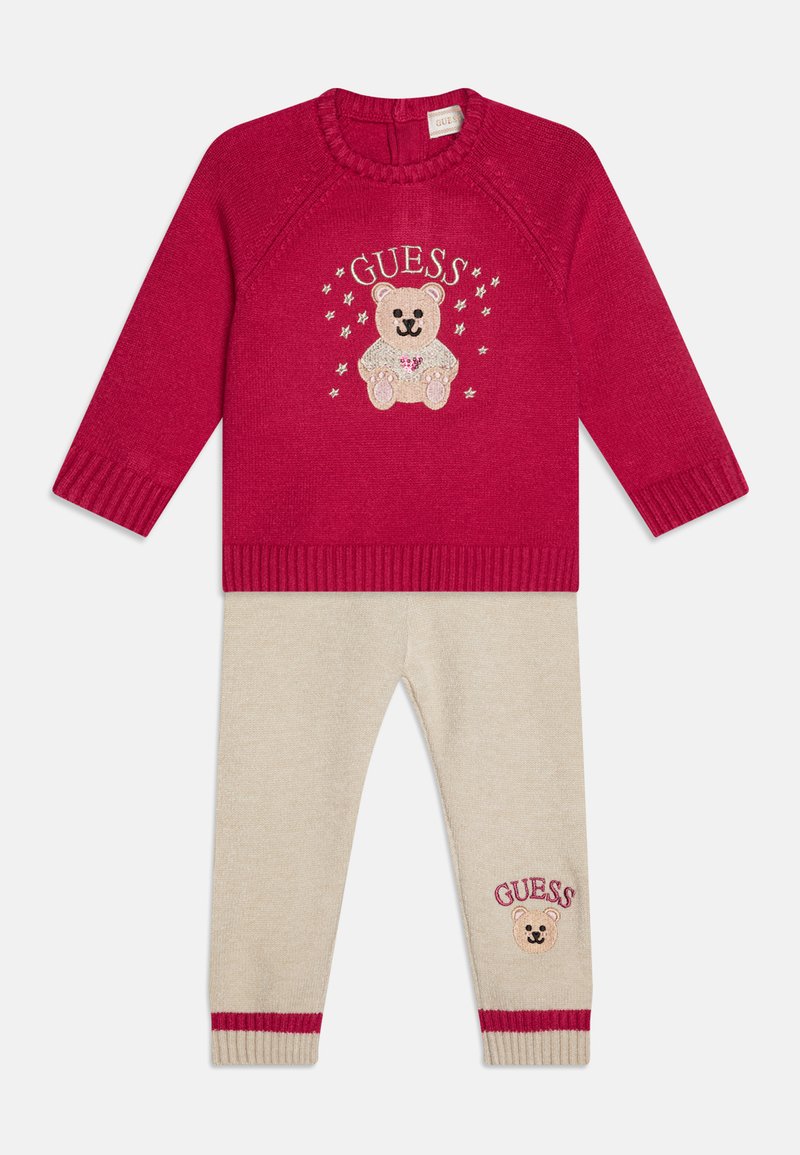 Maglione rosso lavorato a maglia con ricamo di orsetto e stelle, abbinato a pantaloni beige con orlo a righe rosse e un dettaglio di orsetto coordinato.