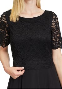 Zwarte kanten top met korte mouwen, bloemenpatroon, golvende zoom. Glad materiaal contrasteert met de gestructureerde kant. De pasvorm is ontspannen rond de taille.