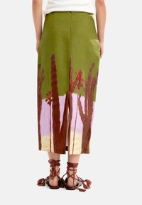 Zielona lniana spódnica z nadrukiem krajobrazu pustyni, z wysokimi kaktusami i kwiatami w odcieniach czerwieni i purpury. Średniej długości z rozcięciem z tyłu.