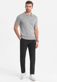 Grijze polo met korte mouwen en geribbelde textuur, gecombineerd met donkere, taps toelopende broek en grijze sneakers. Beide kledingstukken hebben een minimalistisch ontwerp.