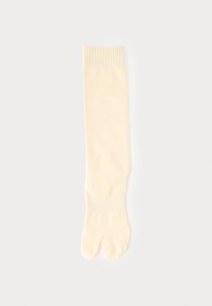 Kremowa skarpeta z rozdzielonym palcem, ściągacze przy górnej krawędzi i kostce, ułożona płasko na jasnym tle.