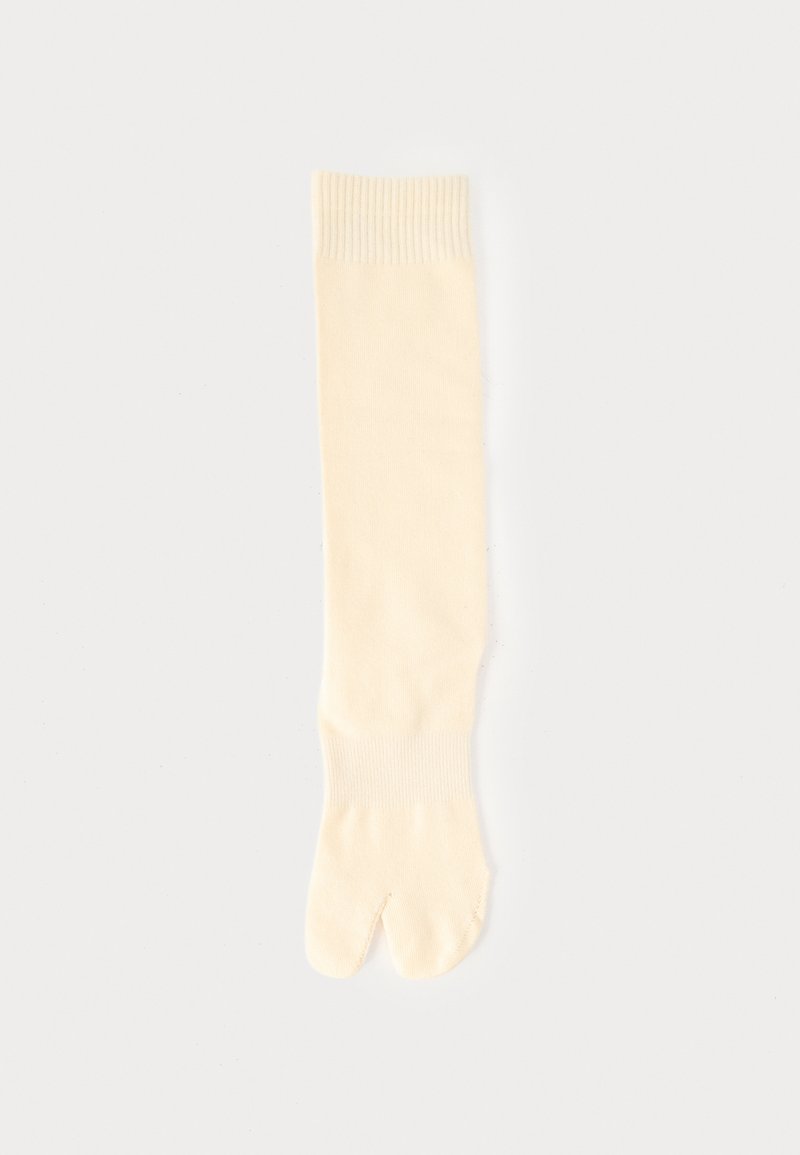 Κρεμ κάλτσα με σχεδιασμό διαχωρισμένου δακτύλου, ριμπ μανσέτες στο πάνω μέρος και στον αστράγαλο, τοποθετημένη επίπεδα σε ανοιχτό φόντο.