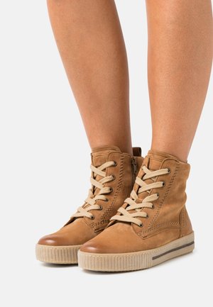 Bruna läderankelboots med en strukturerad ovandel, beige snören och en ribbad gummisula. Siddragkedja för enkel påtagning.