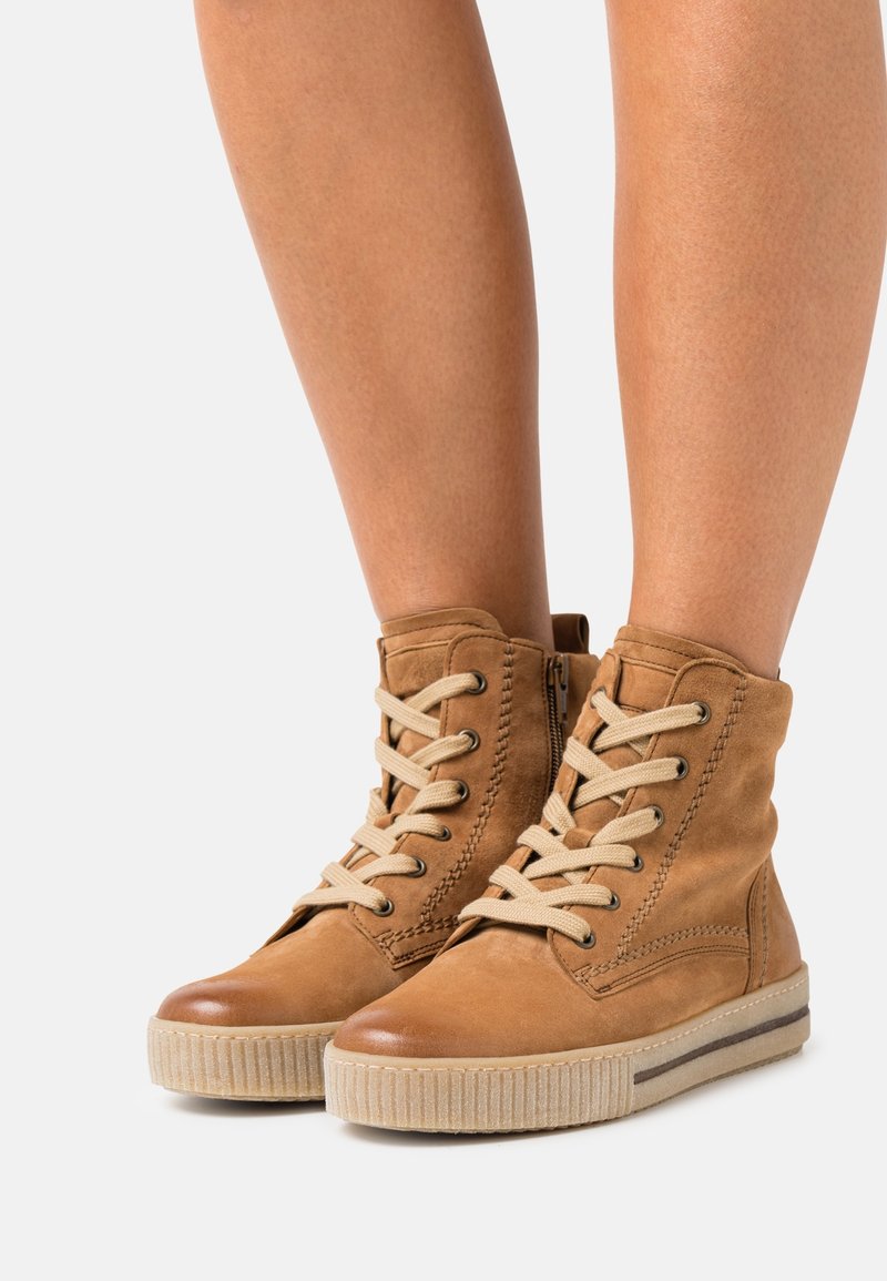 Bottines en cuir tanné avec une tige texturée, lacets beiges et semelle en caoutchouc rainurée. Fermeture éclair sur le côté pour un enfilage facile.