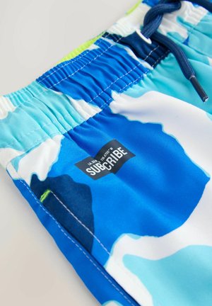 Blaue und weiße gemusterte Badeshorts mit elastischem Bund, Kordelzug und einem schwarzen Etikett mit dem Wort "ABONNIEREN". Glatte Stoffstruktur.