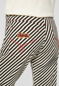 Spodnie w paski z wysokim stanem w kolorze czarnym i kremowym, z czerwonym przeszyciem na kieszeniach oraz kolorowym haftowanym logo.