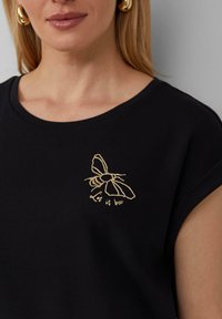 Zwarte T-shirt met korte mouwen, voorzien van een gouden geborduurd bijenlogo met daaronder de tekst "Let it bee". Gemaakt van soepel katoen.
