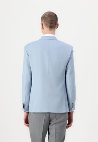 Blazer azul claro hecho de una tela suave, con una sola abertura, ajuste slim y detalles de botones negros en las mangas. Pantalones grises lo complementan.