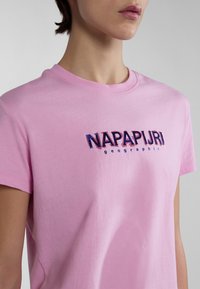 Camiseta de algodón rosa con cuello redondo y mangas cortas, con un logo de "NAPAPIJRI" en azul oscuro y un texto más pequeño "geographic" debajo.