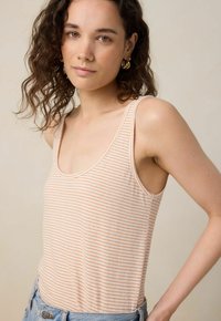 Débardeur rose clair avec de fines rayures orange, fabriqué en tissu doux. Présentant un col théâtre et des bretelles larges pour le confort.