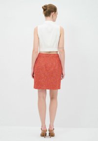 Top blanc sans manches coupé associé à une jupe rouge en tweed ajustée, présentant un motif texturé et une fermeture éclair au dos. Sandales à talons brunes.