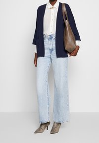 Marinblå cardigan, vit skjorta med knappar, högmidjade ljusblå jeans och ankelboots i ormskinn. Brun axelväska med slät yta.