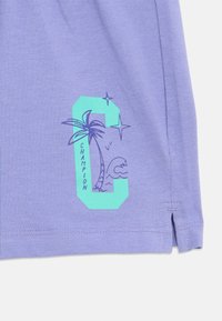 Μωβ ύφασμα με ένα τιρκουάζ γράμμα "C" που απεικονίζει φοίνικα, κύματα, αστέρια και τη λέξη "CHAMPION" τυπωμένη κάθετα.