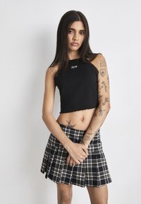 Black cropped tank top with jagged hem and logo detail, paired with a black and white plaid pleated mini skirt.
