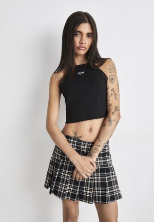 Black cropped tank top with jagged hem and logo detail, paired with a black and white plaid pleated mini skirt.