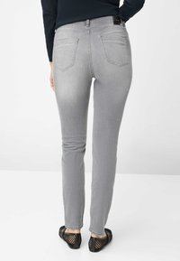 Jeans skinny in denim grigio con due tasche posteriori. Il tessuto ha una texture liscia e un leggero effetto sbiadito. Abbinati a scarpe nere in mesh.