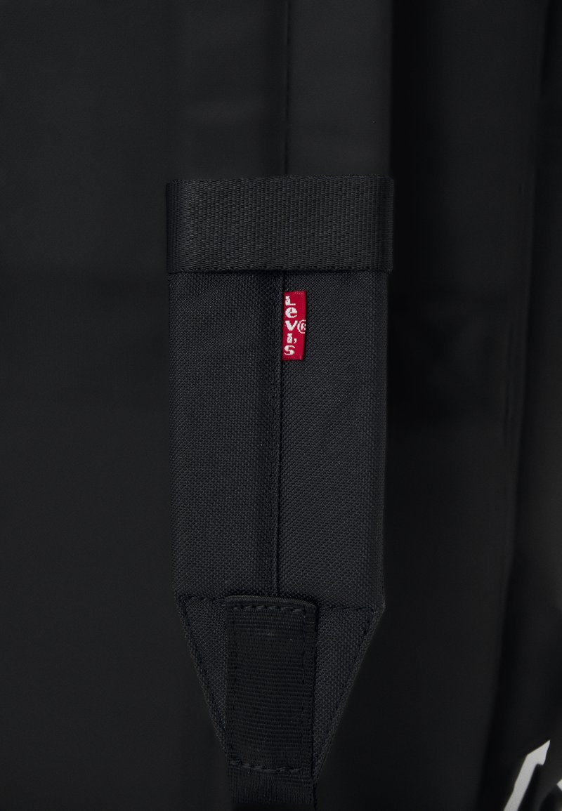 Sort stofpose med en tekstureret overflade, der har et fremtrædende rødt Levi's mærke syet på remmen. Remmen har et stift design.