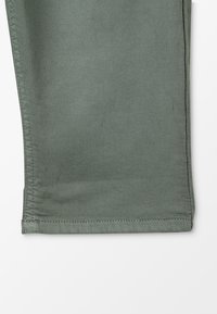 Zielony dół bawełnianych spodni o prostym kroju, widoczne przeszycia i gładka faktura; prezentuje minimalistyczny design.