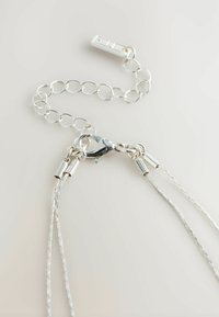 Silvrig kedja halsband lås med förlängningskedja och hummerklor låsare på en ljus bakgrund.