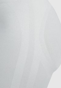 Top sportivo bianco a coste con design senza cuciture, pannelli testurizzati e tessuto liscio, che mette in evidenza un'estetica atletica moderna.
