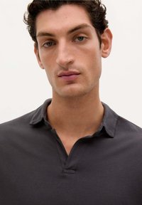 Šedé polo tričko s límečkem, krátkým zapínáním a texturovanou tkaninou. Design je klasický a minimalistický, vhodný pro každodenní nošení.