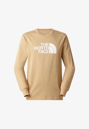 Beige langärmeliges T-Shirt aus Baumwolle mit Rundhalsausschnitt, das vorne ein großes weißes Logo von "THE NORTH FACE" zeigt.