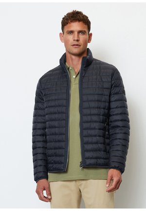 Marineblaue Steppjacke mit hohem Kragen, gestepptem Design und Reißverschluss vorne. Trägt man über einem grünen Poloshirt und verfügt über seitliche Taschen.