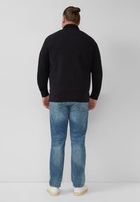 Donkergrijze gebreide trui met een hoge kraag, gecombineerd met lichtblauwe jeans en beige sneakers, gezien vanaf de achterkant.