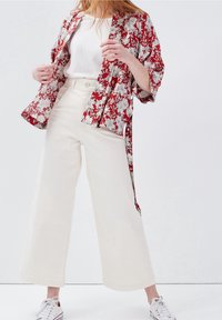 Red floral kimono-style jacket, white tank top, high-waisted cream wide-leg pants, and white sneakers with gray accents.
