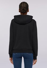 Černá mikina s kapucí, volného střihu, s ribbovanými manžetami a spodním lemem, z měkké textilie, jednoduchý design, nošena s modrými džíny.