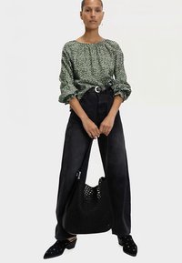 Green floral blouse with gathered neckline and puffed sleeves, paired with high-waisted dark jeans, black woven bag, and black studded mules.