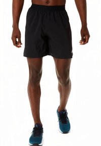 Mustad sportlikud lühikesed püksid elastse vöökohaga, iseloomustatud lõdva istuvuse ja siledapinnaga. Kandmisel sinised pitsidega sportjalatsid.