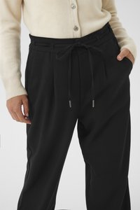 Pantalon noir fuselé avec taille élastique et devant plissé. Le tissu semble doux, avec des accents métalliques aux extrémités des cordons.