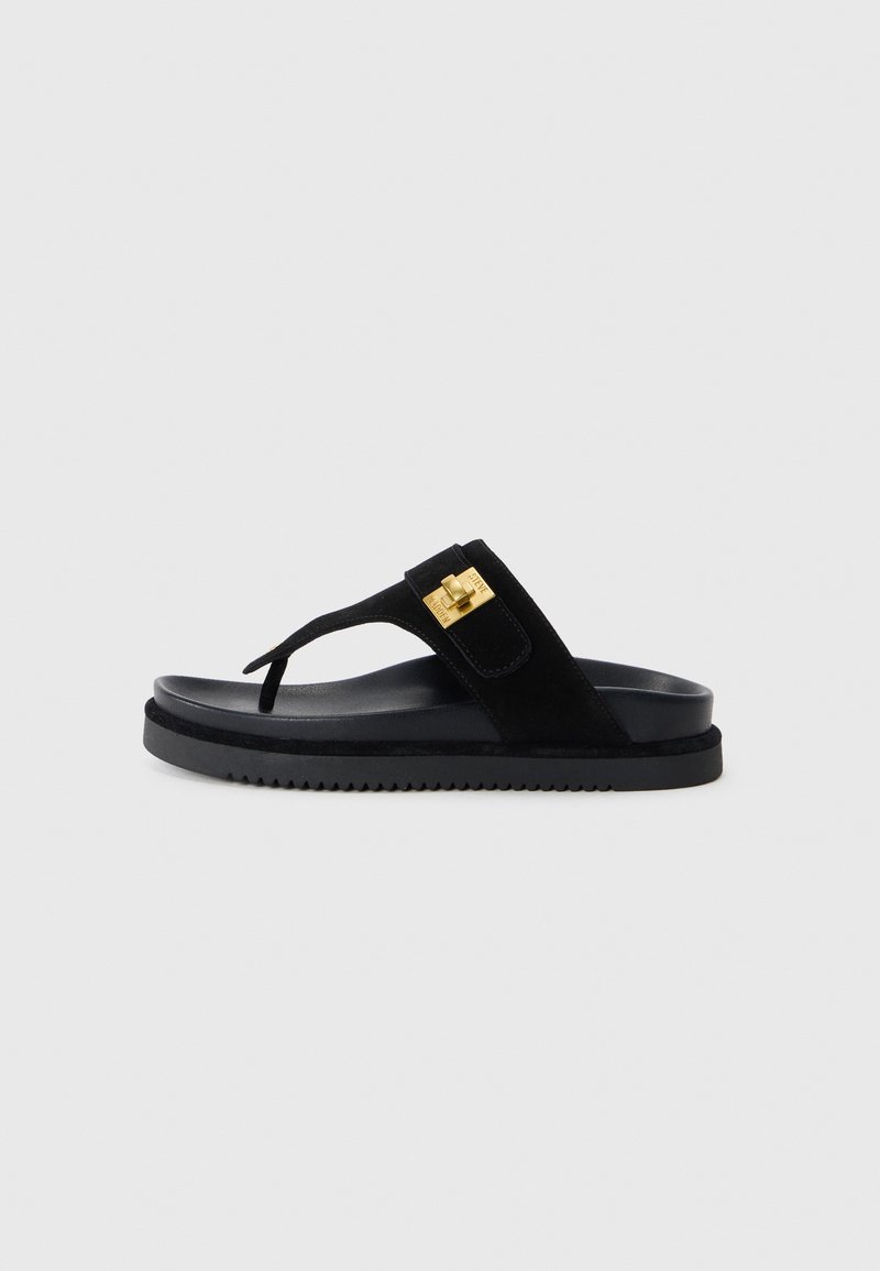 Sandalo flip-flop in suede nero con una suola in gomma nera spessa, caratterizzato da un dettaglio in hardware dorato sulla fascia. Design piatto con texture minima.