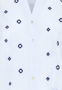 Camicia bianca con bottoni e scollo a V, decorata con piccoli motivi floreali geometrici ricamati di colore blu navy.