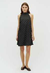 Rochie fără mâneci, neagră, cu buline albe, gât înalt și o ușoară formă A-line. Țesătura fină se așează suav, completând designul.