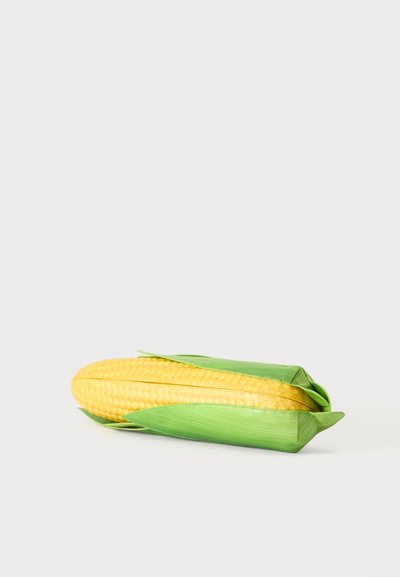 Épi de maïs jaune partiellement enveloppé dans une enveloppe verte sur un fond gris clair, montrant les grains et les feuilles en détail.