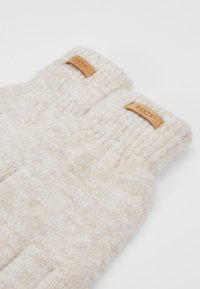 Guantes de punto en color crema con una textura suave. Presentan puños acanalados y pequeñas etiquetas de cuero con el logotipo en relieve "BARTS."