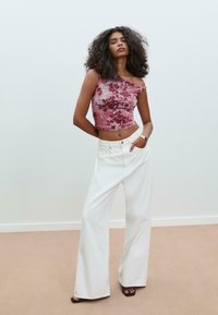 Rosa, blumengemusterte, einseitige Cropped-Top kombiniert mit weißen, weit geschnittenen Jeans. Weicher Stoff mit lockerer Passform. Dunkle Sandalen runden den Look ab.
