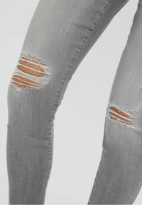 Šedé džínové skinny kalhoty s roztrhanými otvory na kolenou, které ukazují surové okraje a těsný siluetu pro moderní vzhled.
