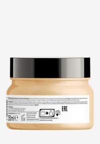 Creamy beige hair mask in a round, translucent jar with a black lid. Contains text and symbols on the label, detailing usage and ingredients.