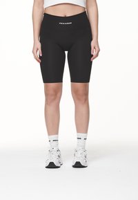 Höga svarta cykelshorts med en jämn yta, logotyp på midjebandet, i kombination med vita strumpor och sneakers.