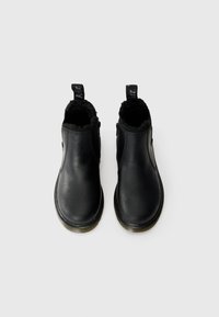 Botas de cano curto em couro preto com um forro suave e peludo, painéis laterais elásticos e alças para facilitar o calçar. Solas de borracha planas com textura.