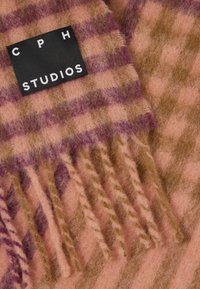 Károvaný šál ze vlny v růžové, béžové a fialové barvě s třásněmi, se černou obdélníkovou nášivkou CPH Studios přišitou na látce.
