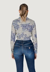 Bloemafdruk, lang употреб shirt in lichtcrème met blauwe en paarse patronen, gecombineerd met hoge taille donkerblauwe jeans met hoekige zakken.