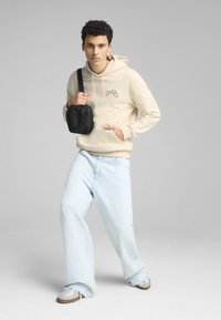 Felpa beige con un design grafico, abbinata a jeans a gamba larga blu chiaro. Il modello porta una piccola borsa a tracolla nera.