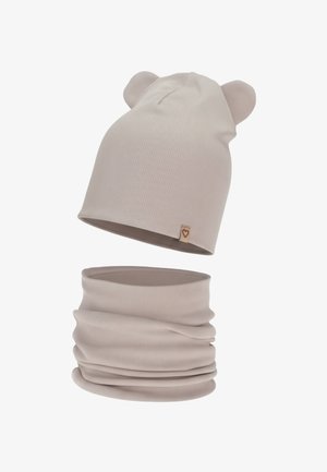 Bonnet en tricot beige clair avec des oreilles d'ours et écharpe tubulaire assortie, présentant une texture côtelée et une petite étiquette en forme de cœur.
