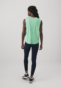 Lys grønn ermeløs topp med en avslappet passform, kombinert med marineblå leggings og svarte joggesko. Glatt stoff med avrundet kant.